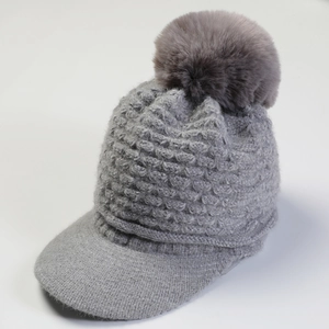 Close-up of gray knit peaked beanie with a fluffy faux fur pom-pom and thick texture