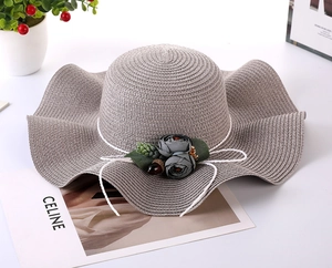 Detail of grey straw sun hat featuring wavy wide brim and elegant floral bow accent