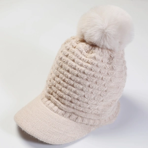 Detail showing the creamy white knitted texture and large faux fur pompom on this winter hat
