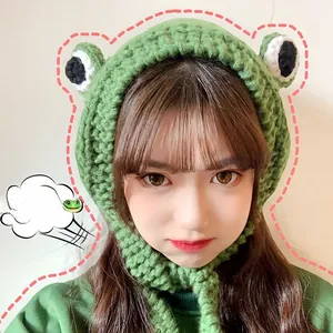 Detailed knit of a green frog-shaped beanie with large eyes and adjustable straps