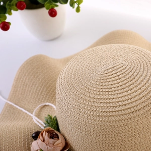 Detail of beige straw hat featuring wave brim, delicate woven texture and fabric floral decor