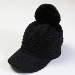 Detail of black knit beanie with visor and large faux fur pompom for winter