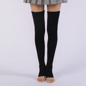 Detailed view of black ribbed knit stirrup leg warmers worn with a pleated skirt