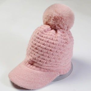 Close-up of pink knit winter hat with fluffy fur pompom and ribbed visor detail