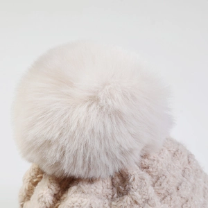 Macro shot of a fluffy faux fur pompom on an oatmeal chunky knit winter beanie cap