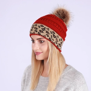 Detail of red knit beanie with leopard print cuff and a fluffy brown faux fur pom pom