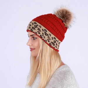 Detail of red cable knit beanie featuring leopard pattern cuff and brown faux fur pompom