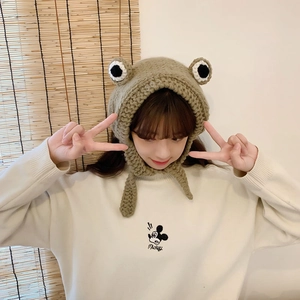 Detail of green knit frog hat with large decorative eyes and side straps for women