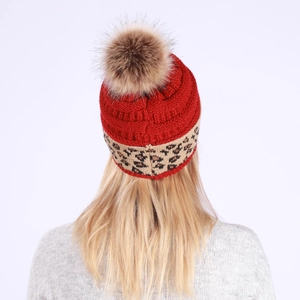 Detail of red knitted beanie featuring a fluffy brown faux fur pompom and leopard band