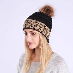 Detail of black knitted beanie featuring leopard print trim and a fluffy faux fur pompom