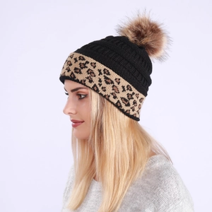 Close-up of leopard print cuff and faux fur pompom on thick knitted winter beanie