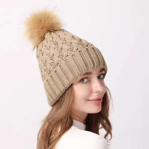 Dettaglio del berretto in maglia a trecce con pompon in ecopelliccia beige
