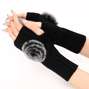 Détail de mitaines en tricot noir avec un grand pompon en fausse fourrure douce