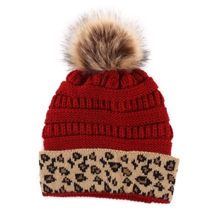 Detail of red cable-knit winter beanie with leopard print cuff and faux fur pom-pom