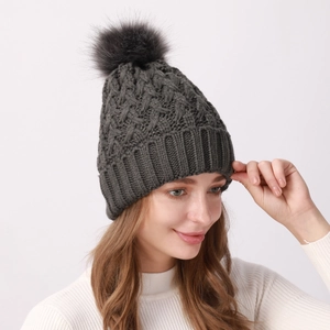Dettaglio del cappello in maglia a trecce grigio scuro con pompon in ecopelliccia