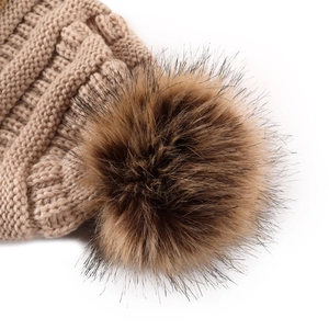 Detailed view of camel knit beanie with thick cable pattern and fluffy faux fur pompom