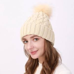 Texture a maglia del berretto in lana beige con grande pompon in ecopelliccia