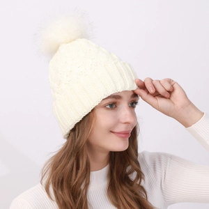 Dettaglio del berretto in maglia bianco avorio con grande pompon in ecopelliccia