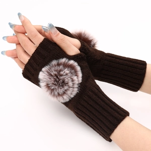 Détail de mitaines en tricot marron foncé avec de grands pompons en fausse fourrure