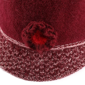 Close-up of deep red knitted flower detail and plush ball texture on winter hat