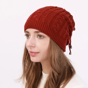 Macro detail of dark red cable-knit texture and metallic drawstring cord ends on the beanie