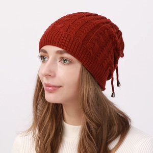 Close-up of deep red cable knit hat featuring a decorative drawstring and metal tips