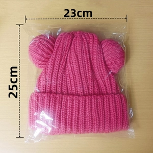 Pink knitted hat with cute bear ears and size dimensions 23cm by 25cm on wooden surface