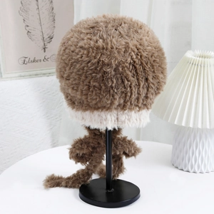 Dettaglio del cappello in peluche marrone con bordo bianco e nappe in maglia