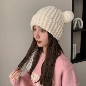 Close-up detail of cream white knitted beanie with cute bear ears and vertical texture