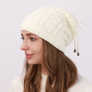 Detail of cream cable-knit beanie featuring adjustable drawstring and silver metal charms