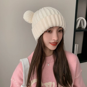Detail of white chunky knit beanie with bear ears worn by model for winter warmth