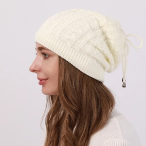 Detail view of cream cable-knit beanie featuring adjustable drawstring with metal pendant