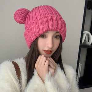 Detail of a thick pink knitted beanie with bear ear poms and warm ribbed texture