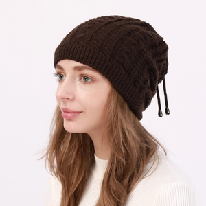 Detail of dark brown cable-knit beanie with metal buckle drawstring and soft winter texture