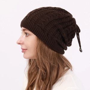 Detail of dark brown cable knit beanie with thick texture and decorative drawstring bead