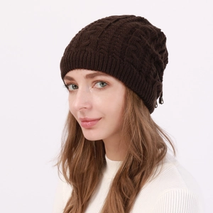 Detailed close-up of dark brown cable knit texture and metal charm on beanie