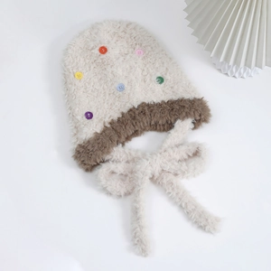 Dettaglio cappello in peluche beige con bottoni colorati e lacci in pelliccia