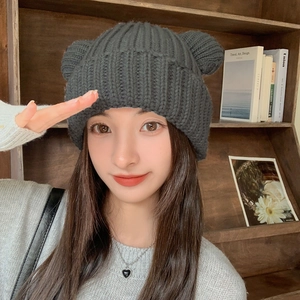 Close-up of dark grey thick knit beanie with cute bear ears on soft textured fabric