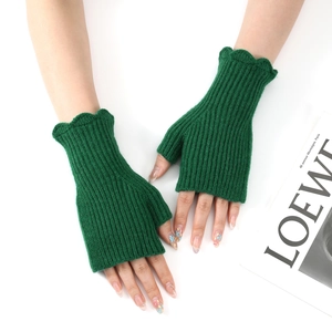Detail view of green knitted fingerless gloves with elegant ruffle trim on a white surface