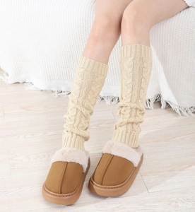 Close-up of thick cable knit leg warmers in cream paired with brown fur-lined slippers