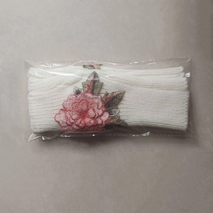 Détail de mitaines en tricot blanc avec broderie de fleurs roses sous emballage plastique