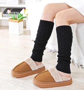 Close-up of black cable-knit leg warmers paired with cozy brown plush slippers