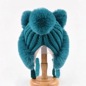Close-up of teal knit beanie with faux fur pom-poms and warm plush lining detail