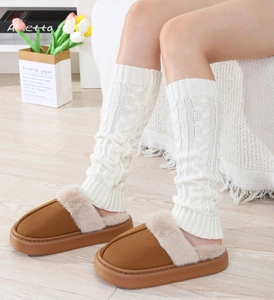Close-up of thick cable knit leg warmers in white with fuzzy brown indoor slippers