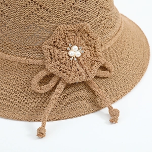 Close-up of beige straw sun hat featuring woven floral accent with pearls and crystals