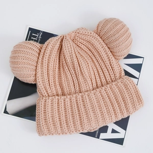 Detail of pink knitted baby hat featuring large pom-poms and thick warm texture