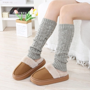 Detail of light gray cable knit leg warmers paired with cozy brown plush slippers