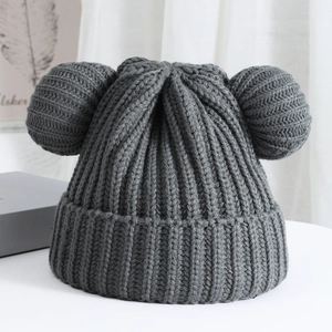 Detailed knit texture of dark grey beanie with cute bear ear pom-poms on a white table