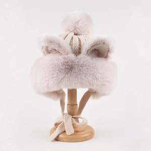 Detail of plush beige earflap hat featuring cute cat ears and a soft pom-pom top