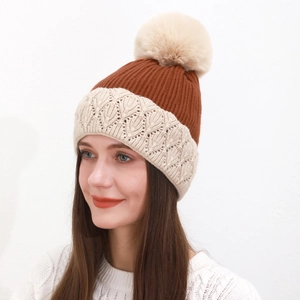 Dettaglio del berretto in maglia con motivi bicolore e un grande pompon in ecopelliccia beige
